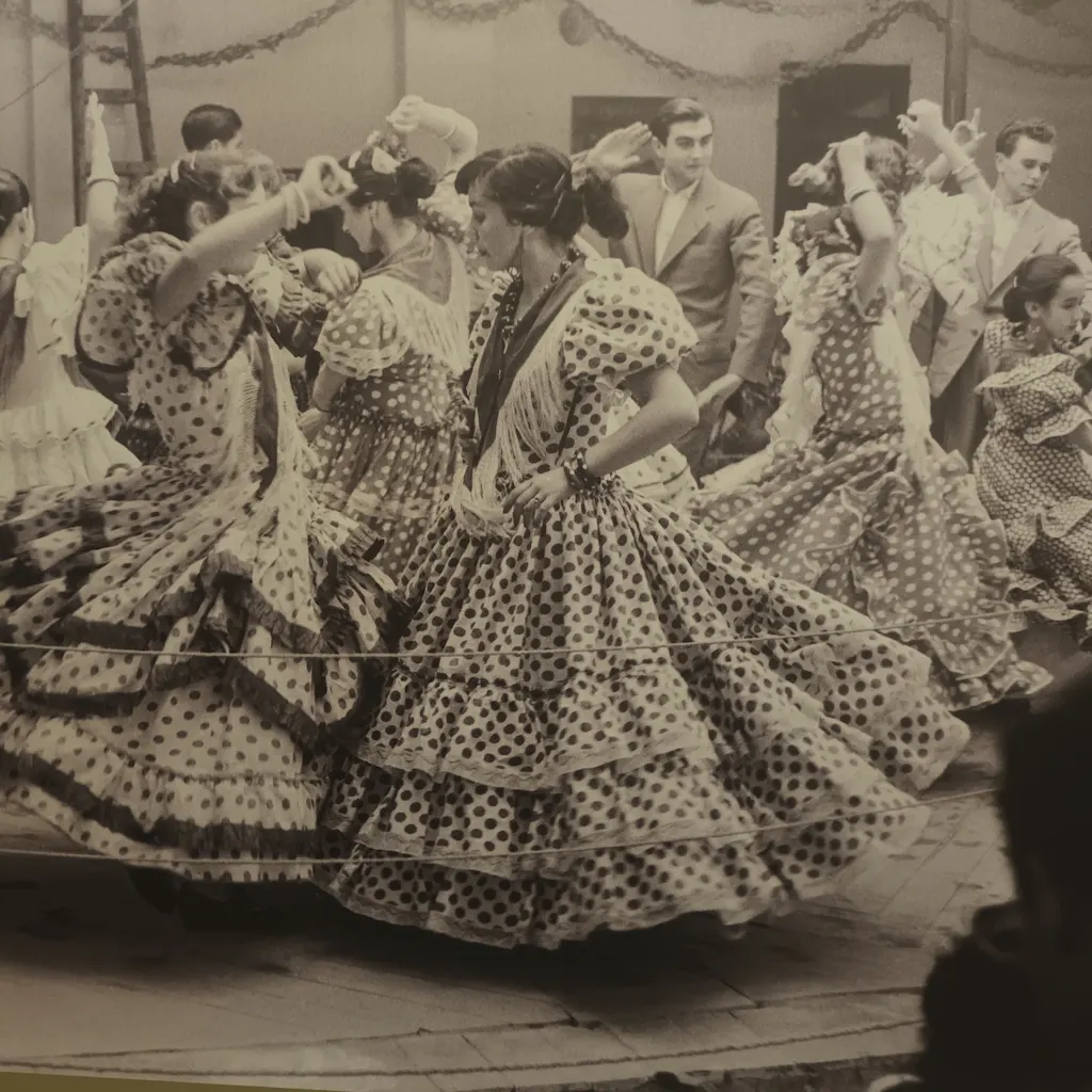 Foto antica di un ballo di sevillana. Donne con tipico vestito con balze e pois ballano in coppia.