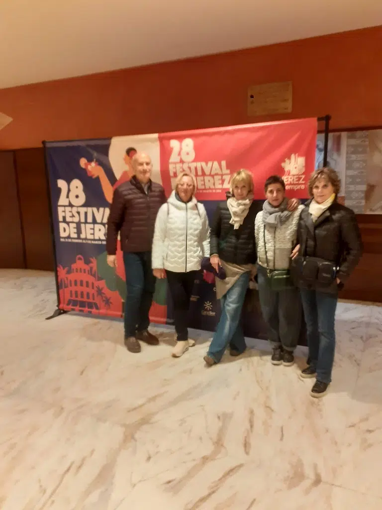 In questa foto, cinque persone sorridenti nella hall del teatro posano davanti al colorato sfondo promozionale del 28° Festival de Jerez. L'atmosfera è accogliente e gioiosa, con tonalità vivaci di rosso e blu sullo sfondo che enfatizzano l'importanza del festival